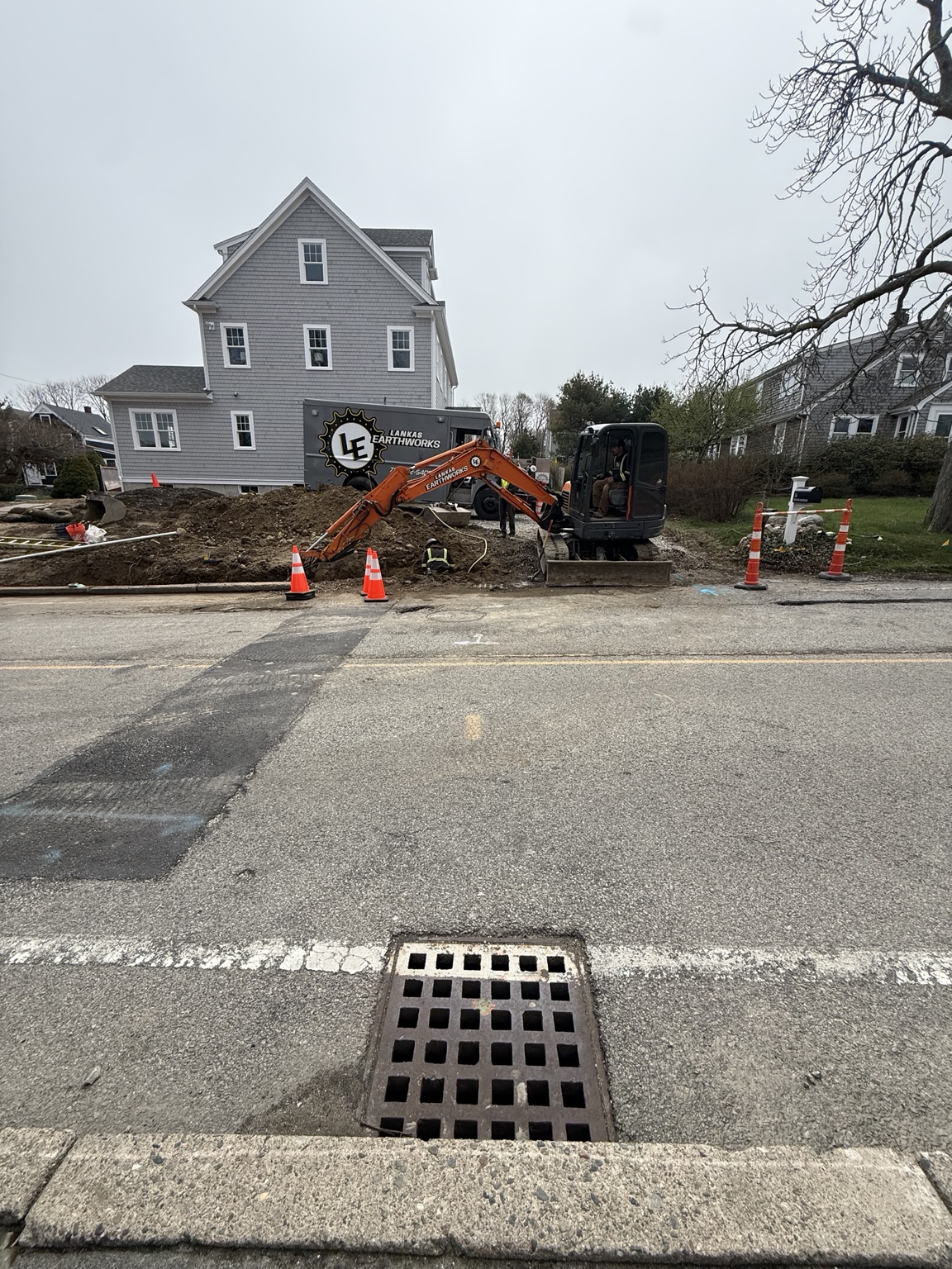 Excavator and crew completing utility work beside a residential street